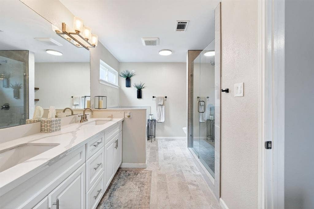 Dual vanity with undermount sinks and light-toned countertops, expansive mirror, clear glass shower enclosure, and light-toned flooring