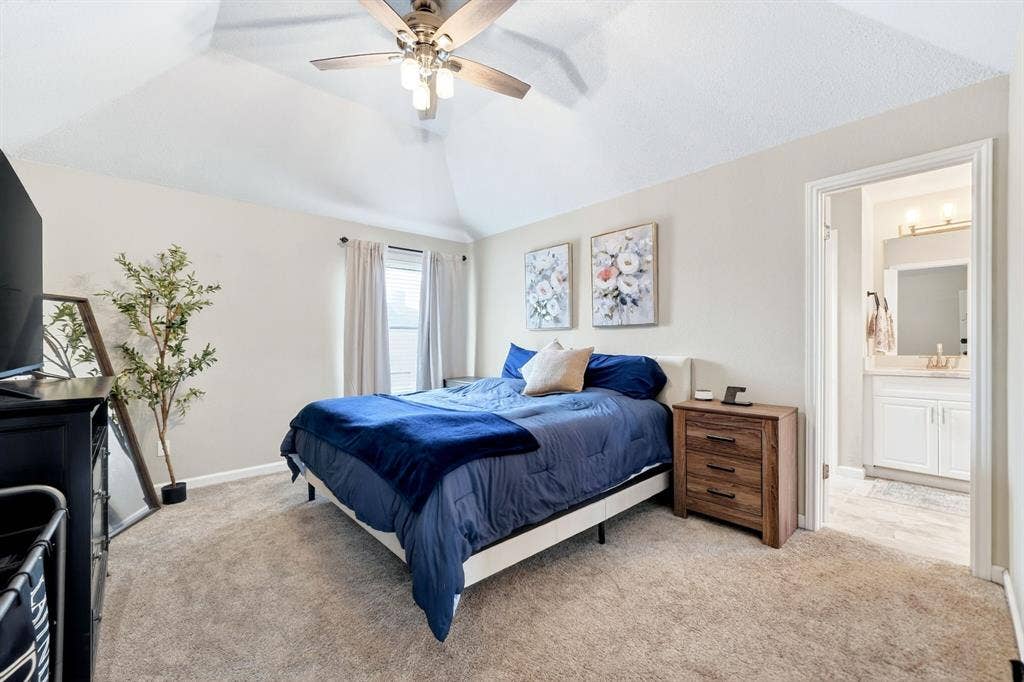Vaulted ceiling with ceiling fan, recessed window, carpeted flooring, and an adjoining bathroom with a vanity and wall-mounted lighting