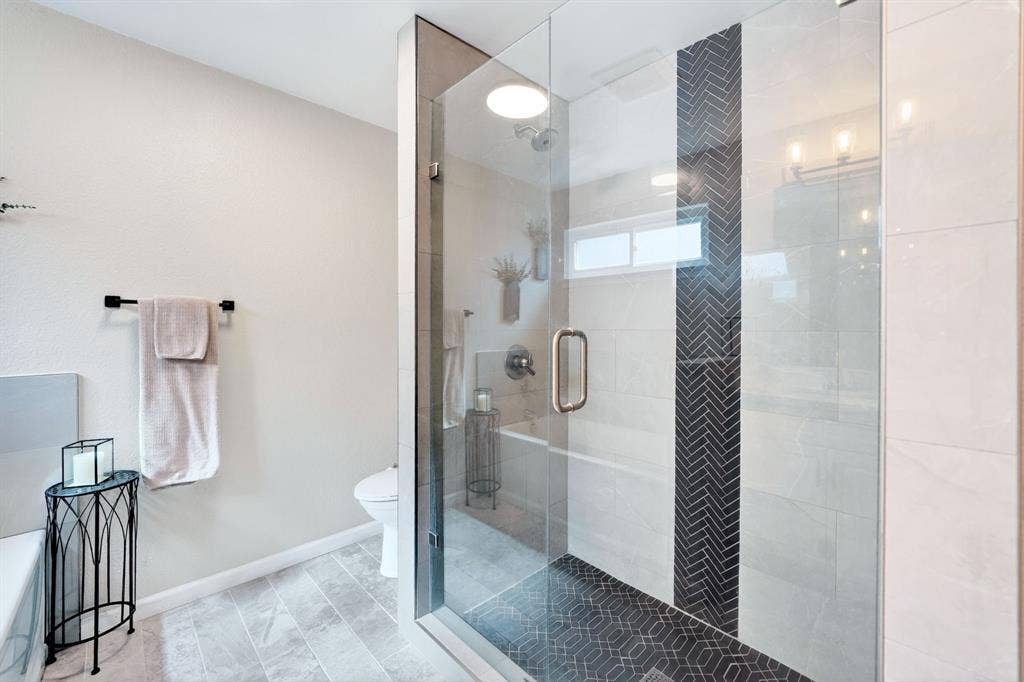 Glass-enclosed shower with black herringbone accent tile and hexagonal mosaic floor