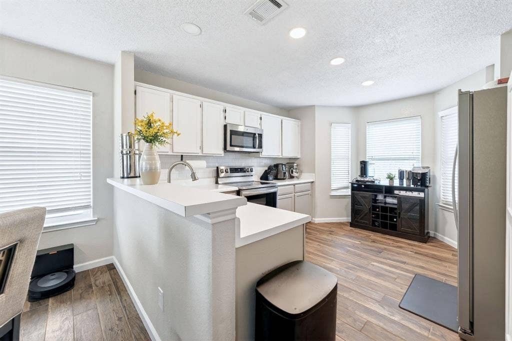 White cabinetry, stainless steel appliances, wood-finish flooring, recessed lighting, and a kitchen island with a breakfast bar