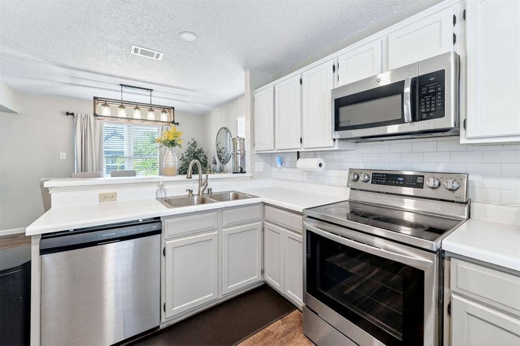 Stainless steel appliances, white cabinetry, white countertops, subway tile backsplash, and a double basin sink