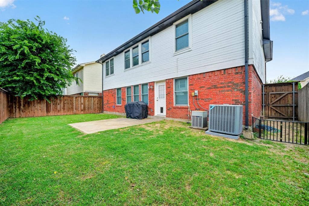 Expansive lawn area with a concrete patio, wood privacy fencing, and a brick and siding exterior