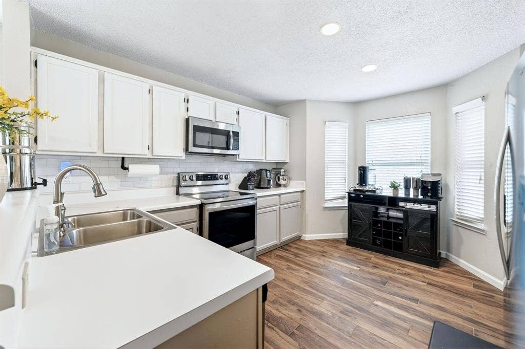 Stainless steel appliances, white cabinetry, wood-finish flooring, recessed lighting, and a subway tile backsplash