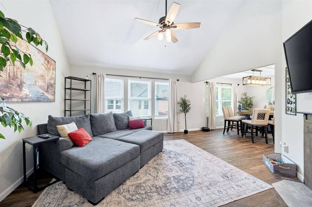 Vaulted ceiling with a ceiling fan, wood-finish flooring, multiple windows with blinds, and an open concept layout