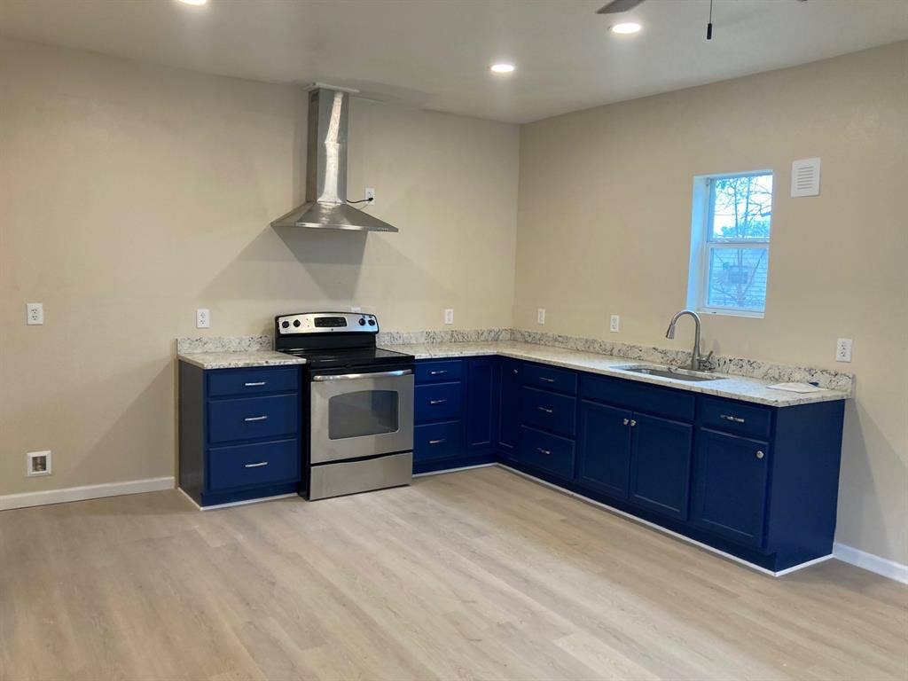 608 Turner Street, Waco, TX 76704 L-shaped kitchen featuring blue cabinetry, light-toned countertops, and stainless steel appliances including a range with an overhead vent hood