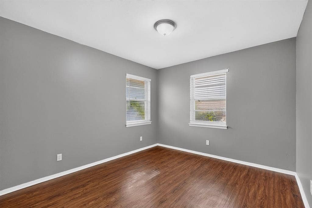101 Spinner Circle, DeSoto, TX 75115 Wood-finish flooring with white trim, two windows with blinds, and neutral grey walls