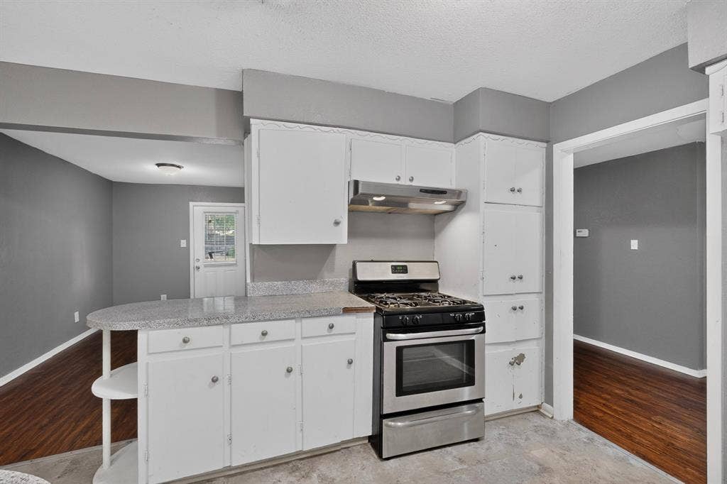 101 Spinner Circle, DeSoto, TX 75115 Modern kitchen featuring white cabinetry with ample storage, stainless steel gas range with convection oven, stainless steel range hood, granite countertops, and wood-finish flooring throughout the open layout