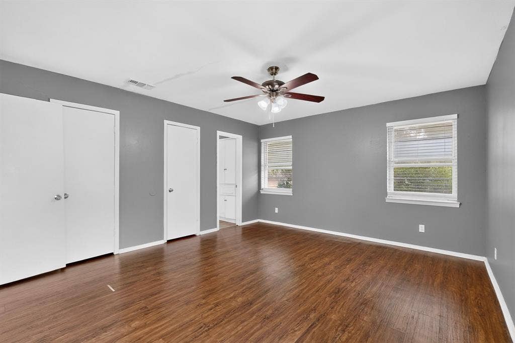 101 Spinner Circle, DeSoto, TX 75115 Spacious bedroom showcasing warm wood-finish flooring, ceiling fan with integrated lighting, and multiple white-painted closet doors