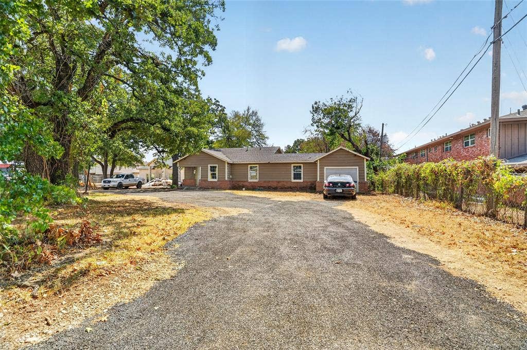 5800 Dallas Avenue, Fort Worth, TX 76112 Single-story residence featuring a gravel driveway, attached garage, and mature trees
