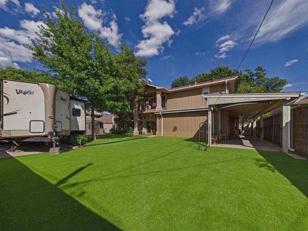9335 Whittenburg Gate, Dallas, TX 75243 Expansive artificial turf lawn, covered patio area, vertical wood-finish siding, and mature trees providing natural screening