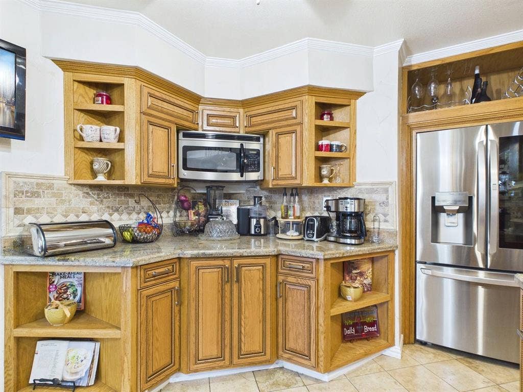 9335 Whittenburg Gate, Dallas, TX 75243 Wood-finish cabinetry with display shelving, stone-finish countertops, tile backsplash, and stainless steel appliances