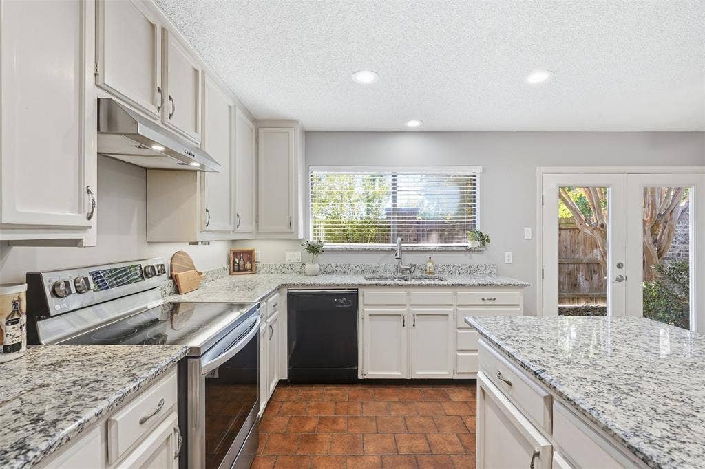 White cabinetry, granite countertops, tile flooring, recessed lighting, and a stainless steel range hood