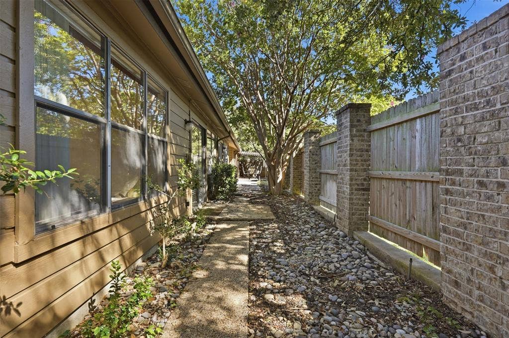 Stone pathway with surrounding river rock, wood siding exterior, multi-pane windows, and a brick and wood fence