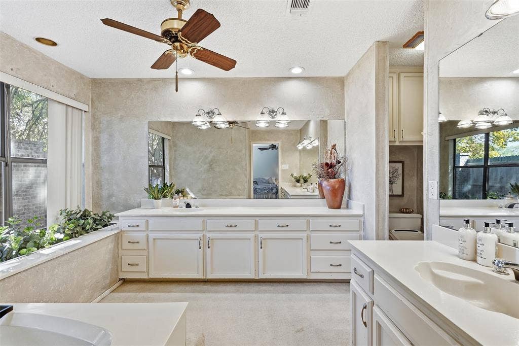 Dual vanity with white cabinetry and integrated sinks, extensive mirror, recessed lighting, and a ceiling fan