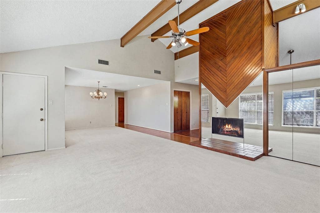 Vaulted ceiling with exposed wood beams, wood-paneled fireplace, mirrored accent wall, and a ceiling fan