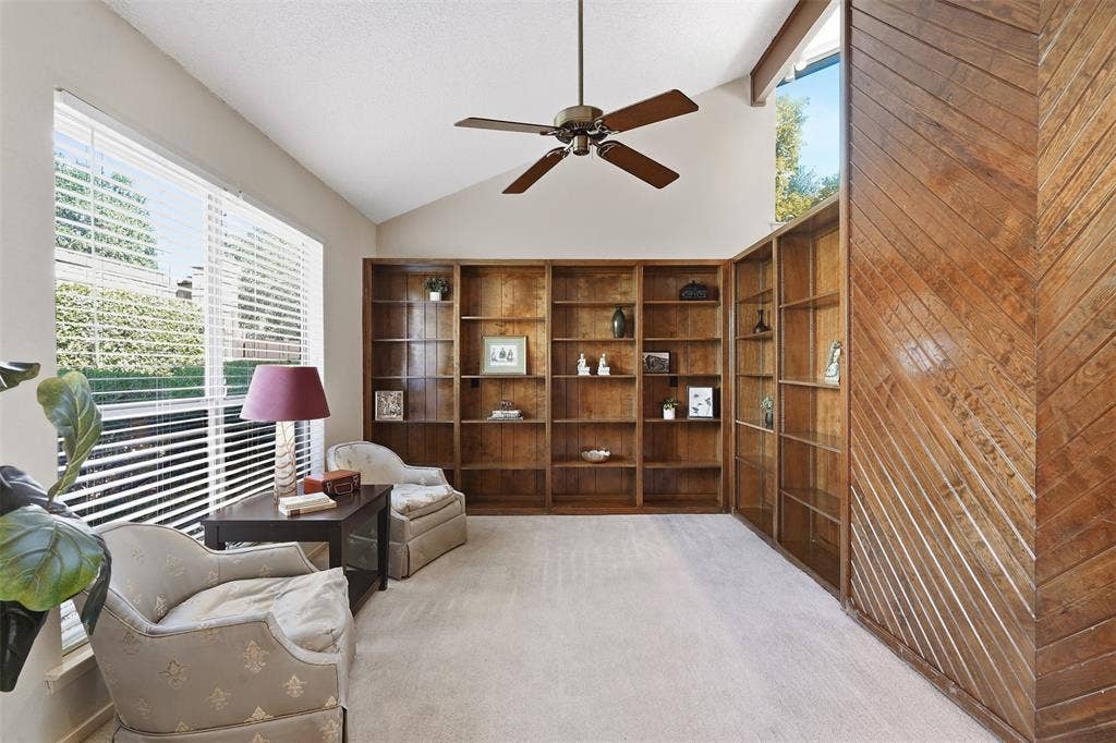 Vaulted ceiling with an exposed beam, ceiling fan, and extensive built-in wooden shelving