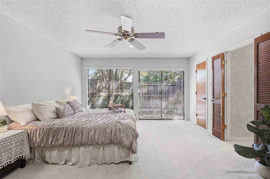 Dual sliding glass doors with horizontal blinds, ceiling fan with light fixture, light-toned carpeting, and wood-finish doors