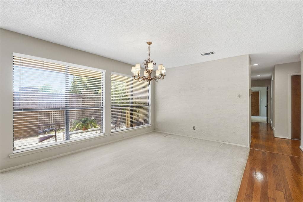 Bright room featuring multiple windows with horizontal blinds, a decorative chandelier, and a combination of carpet and wood-finish flooring