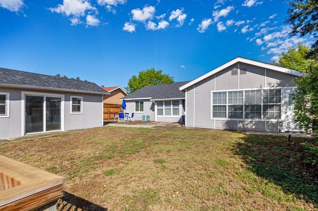 Irving, TX 75060 Backyard featuring a secondary structure with sliding glass doors, a main residence with multiple windows, and a wood-finish deck element