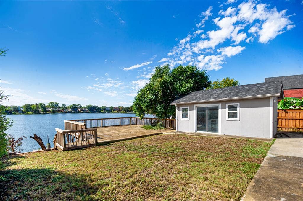 Irving, TX 75060 Waterfront property featuring a large wooden deck, a separate utility building with sliding glass doors, and a concrete pathway