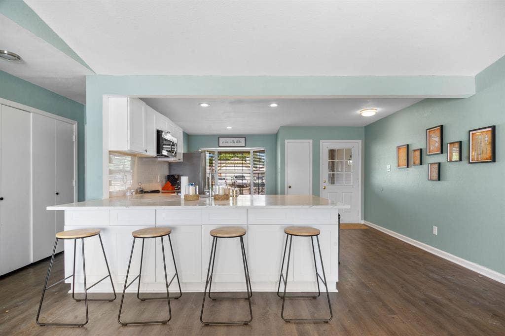 Irving, TX 75060 Kitchen island with light-toned countertop, white cabinetry, integrated stainless steel microwave, and wood-finish flooring