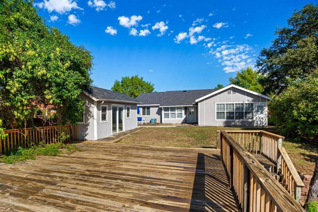 Irving, TX 75060 Expansive wooden deck with railing, detached structure with sliding glass doors, and a main residence featuring multiple windows