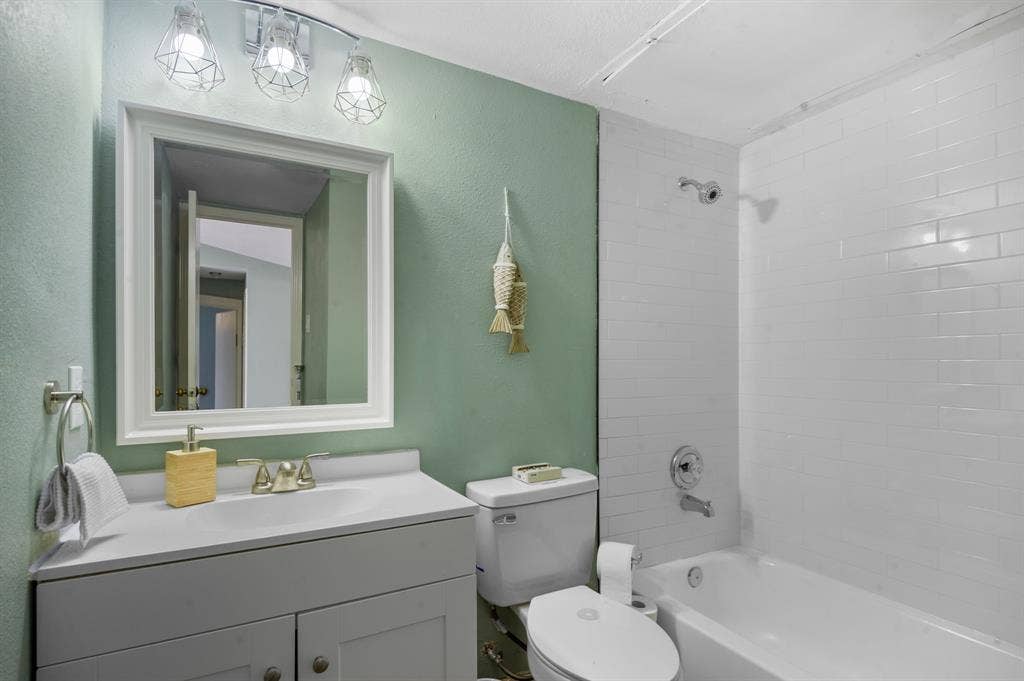 Irving, TX 75060 White vanity with integrated sink and brushed nickel faucet, framed mirror, three-light vanity fixture, white subway tile shower surround, and white bathtub