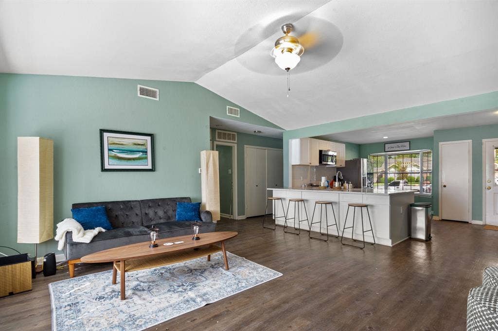Irving, TX 75060 Vaulted ceiling, wood-finish flooring, kitchen island with seating, stainless steel appliances, and white cabinetry
