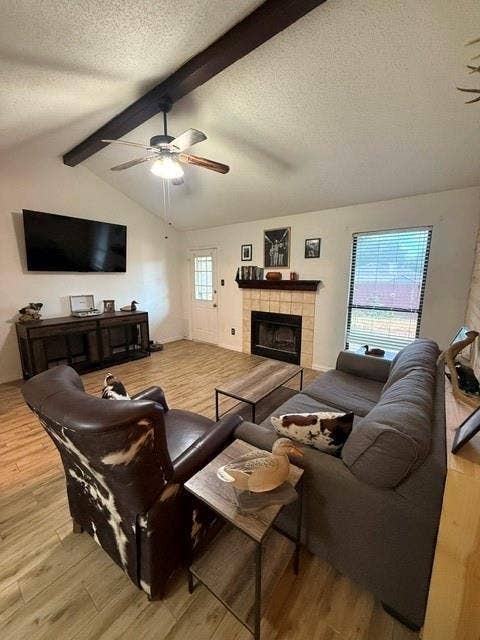 Ceiling with exposed wood beam, wood-finish flooring, fireplace and a ceiling fan