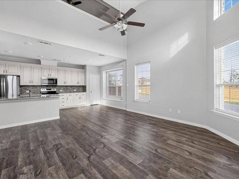 Open-concept living area featuring high vaulted ceilings, wood-finish flooring, and multiple windows with blinds