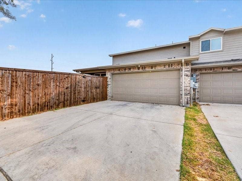 Exterior featuring a two-car garage, concrete driveway, and wood privacy fencing