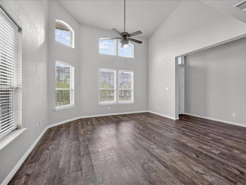 Vaulted ceiling with a ceiling fan, multiple windows, wood-finish flooring, and light-toned wall finishes