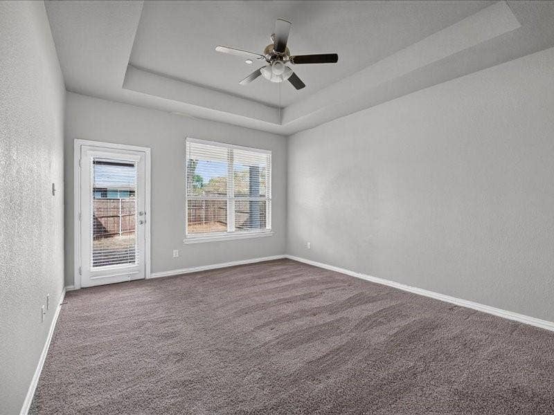 Tray ceiling with a ceiling fan, carpeted flooring, window with blinds, and a glass-paneled door