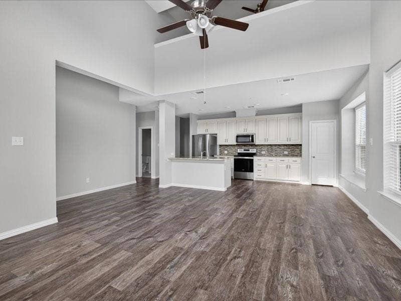 Vaulted ceiling with dual ceiling fans, wood-finish flooring, white kitchen cabinetry, stainless steel appliances, and a textured tile backsplash