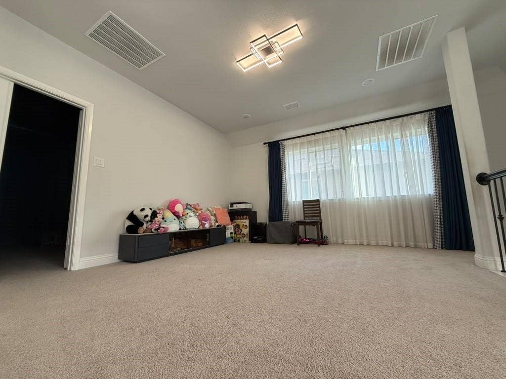 Spacious carpeted Game room featuring a large window with sheers, a modern ceiling light fixture, and white walls