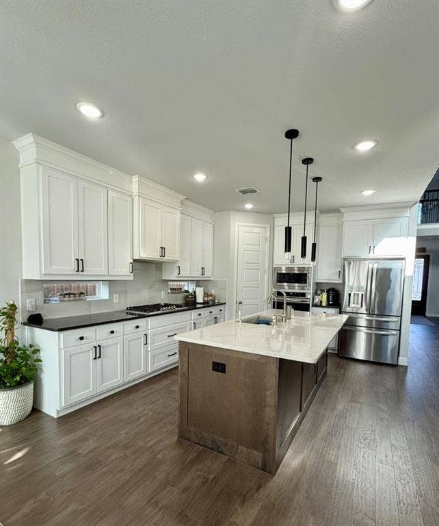Spacious kitchen featuring white shaker-style cabinetry, dark countertops, a large island with light-toned countertop, stainless steel appliances, and wood-finish flooring