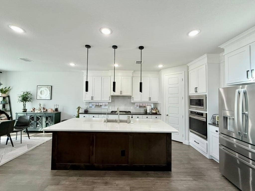 Spacious kitchen featuring an expansive center island with dual sinks, white shaker cabinetry, stainless steel appliances, and wood-finish flooring