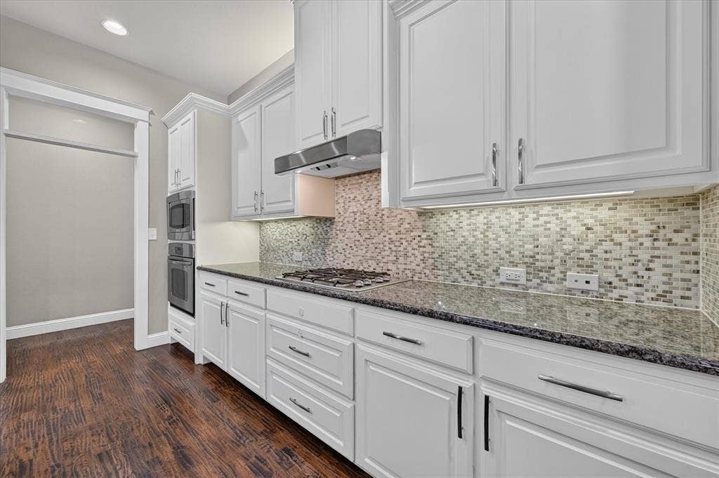 Kitchen featuring white cabinetry, dark stone countertops, mosaic tile backsplash, stainless steel appliances, and wood-finish flooring