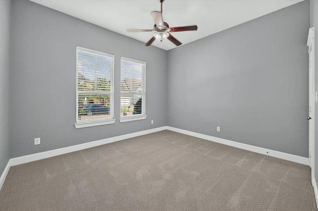 Dual windows with horizontal blinds, overhead ceiling fan with light fixture, gray wall paint, and neutral tone carpet flooring