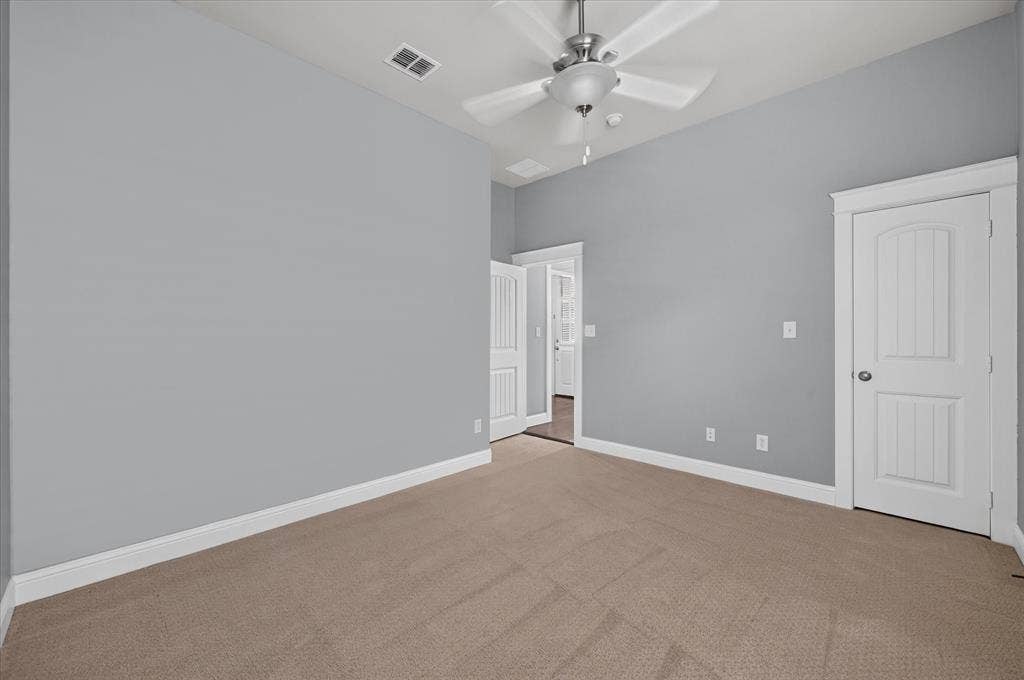 Neutral tone wall paint with white trim, brown carpet flooring, and a ceiling fan with integrated lighting