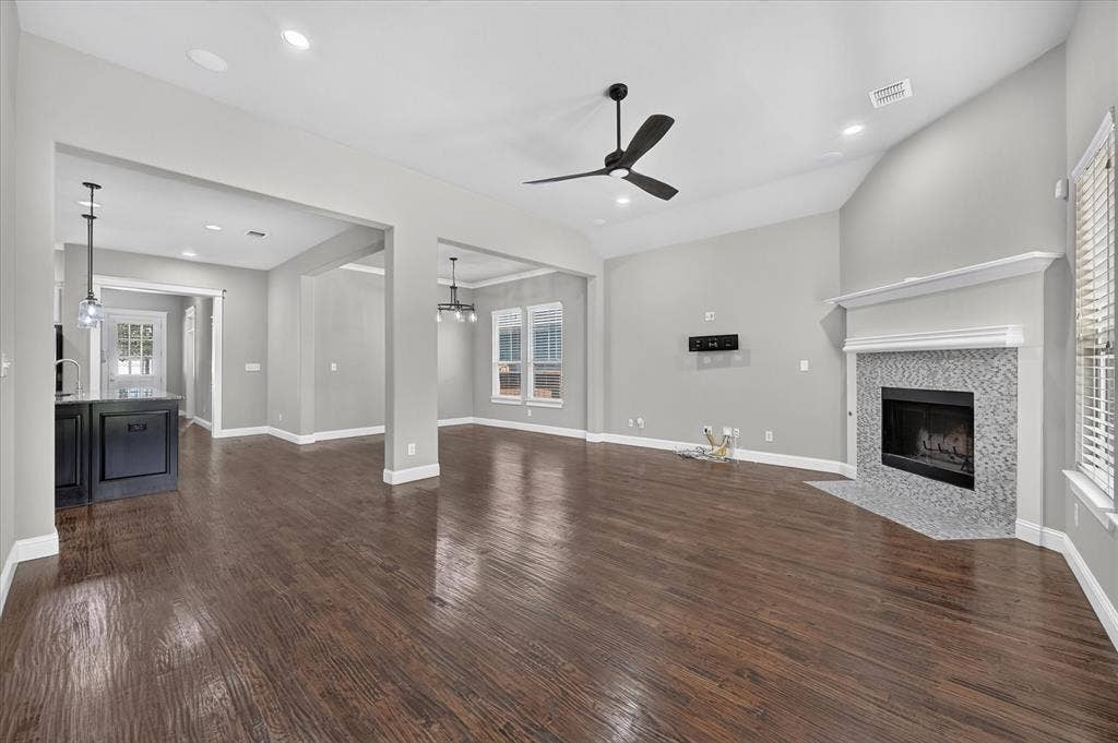 Vaulted ceiling with a ceiling fan, recessed lighting, wood-finish flooring, fireplace with tile surround, and built-in window blinds