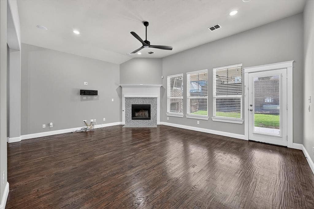 Vaulted ceiling with a ceiling fan, fireplace with a tile surround and mantle, wood-finish flooring, and multiple windows with blinds
