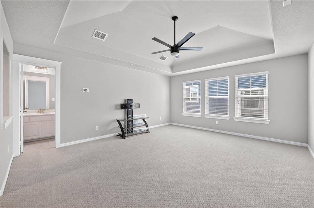 Tray ceiling with a ceiling fan, three windows with blinds, and light-toned carpeting