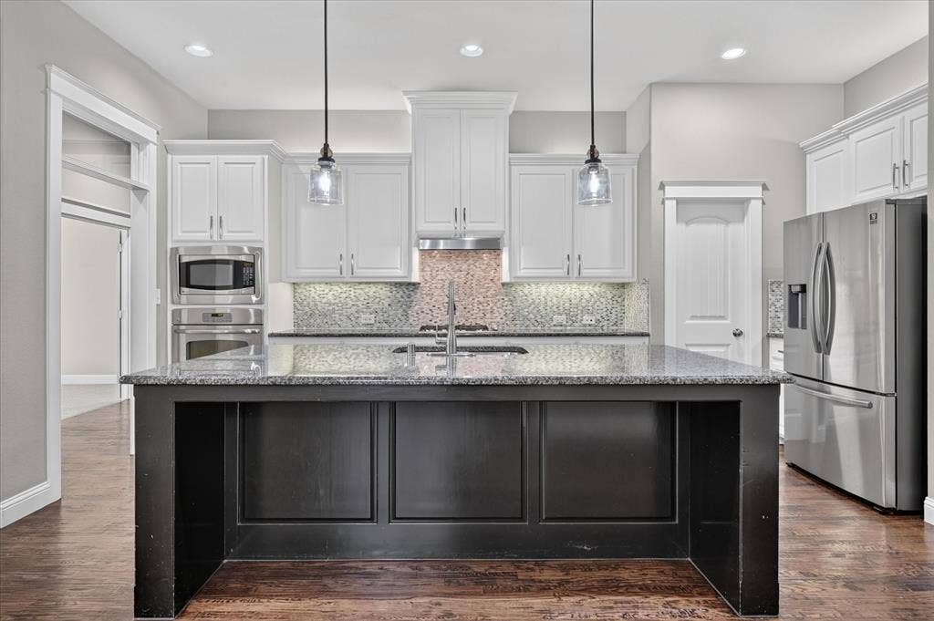 Kitchen featuring a dark-toned island with a built-in sink, stainless steel appliances, white cabinetry, and recessed lighting