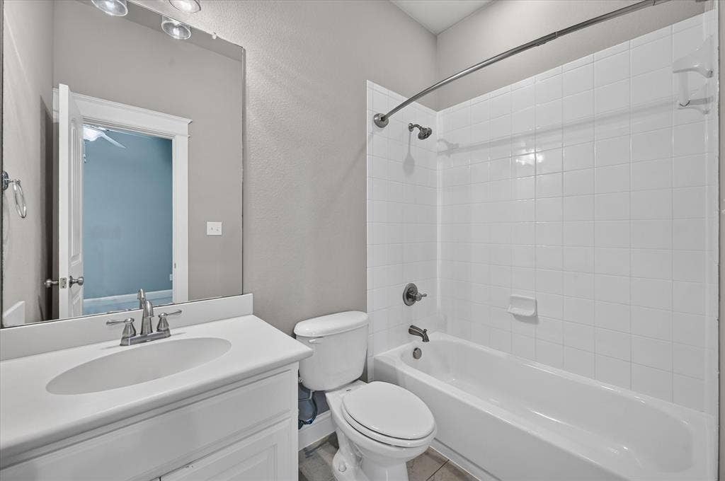 White tile tub/shower combination, single vanity with integrated sink, chrome faucet, and overhead vanity lighting