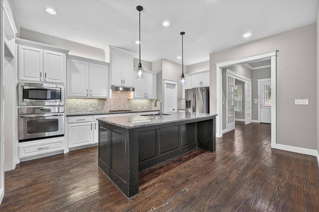 Wood-finish flooring, white cabinetry, stainless steel appliances, central island with dark cabinetry, and pendant lighting