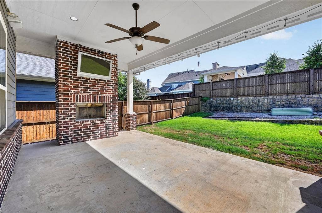 Covered patio with a brick-clad fireplace, integrated ceiling fan, and concrete flooring