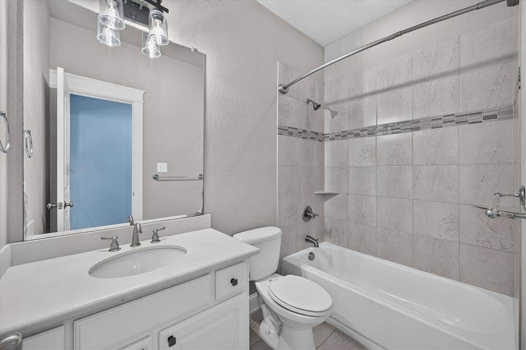 Bathroom featuring a white vanity with an integrated sink, brushed nickel fixtures, a framed mirror, and a tiled shower-tub combination with a decorative accent band
