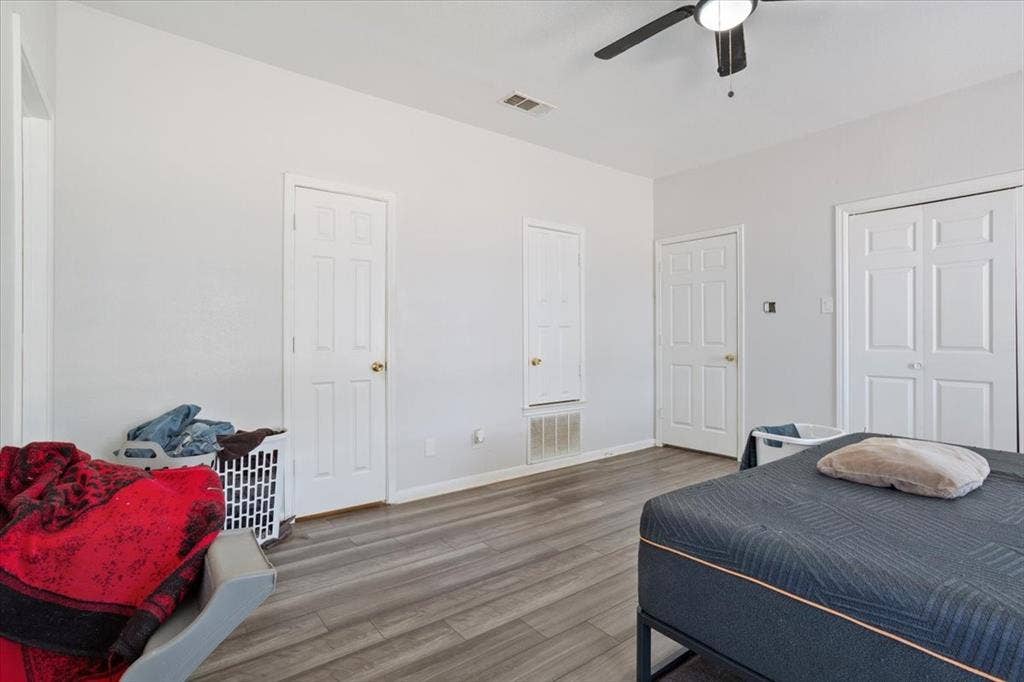 Wood-finish flooring, white walls, white paneled doors, and a ceiling fan with integrated lighting