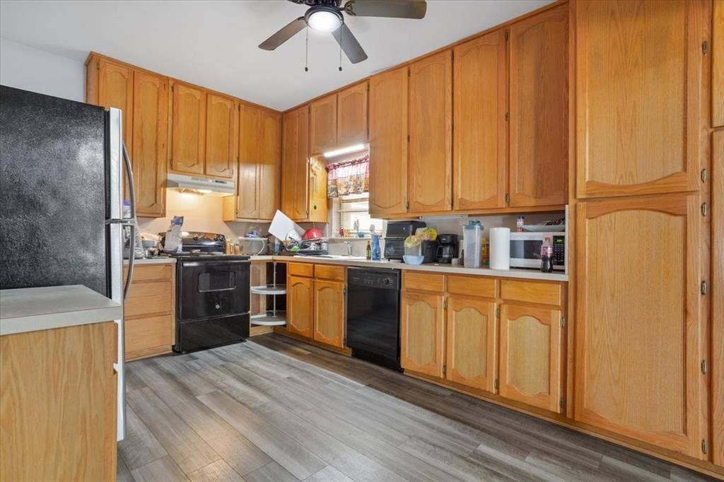 Wood-finish flooring, ample wood cabinetry, light-colored countertops, and ceiling fan